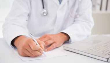 médico de jaleco e estetoscópio no pescoço, escrevendo em um papel branco