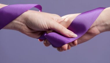 Foto de duas mãos femininas com uma fita lilás levemente solta conectando elas em um fundo lilás escuro