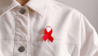 Homem de camisa de botões branca com pequeno laço vermelho dobrado na altura do peito, simbolizando a solidariedade e comprometimento na luta contra a AIDS